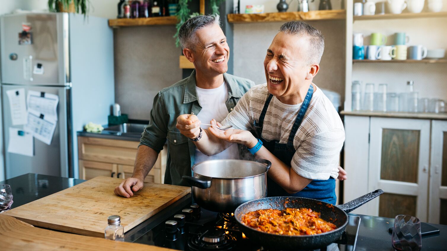 Mid adult cheerful gay couple talking and having fun while cooking in a kitchen