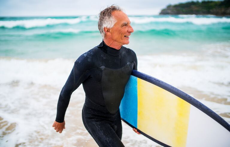 A senior man in wetsuit carrying surfboard on the beach. Bondi Beach, Sydney, Australia