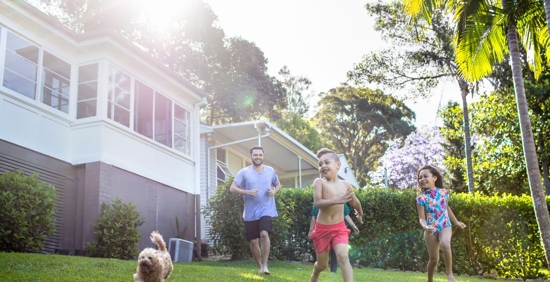 Australian aboriginal family enjoying in the front yard at home on a sunny day, kids are running with their dog and parents are in the background.