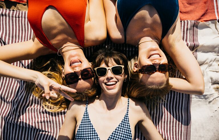 Above view of three women in swimsuits and sunglasses having a sunbath at the beach