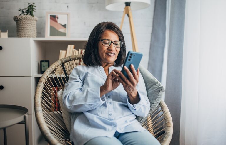 Mature black woman using smart phone while sitting in living room at home.