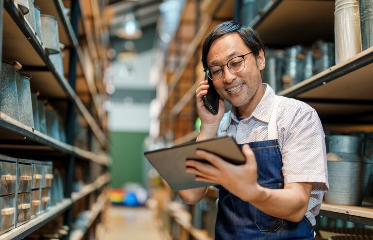 Japanese man shop owner in his store warehouse using mobile phone and tablet confirm online order received correctly with customer. Small business owner at work. Small business local craft product. Online shopping concept.