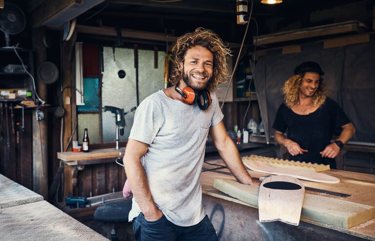 Portrait of two happy young men working on skateboards in their workshop