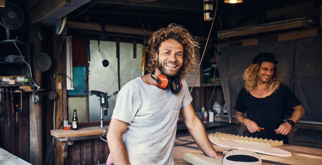 Portrait of two happy young men working on skateboards in their workshop