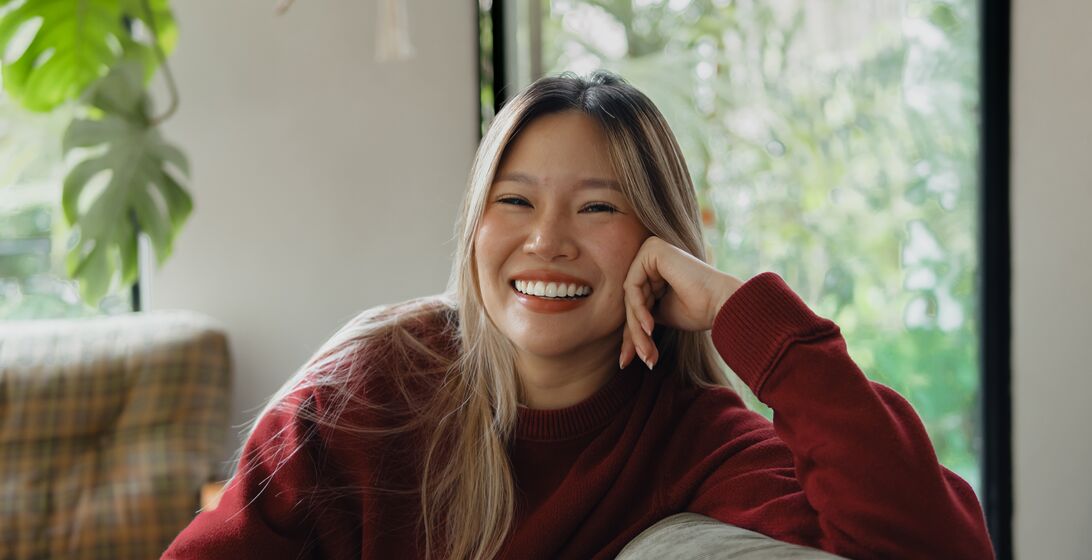 Happy young woman sitting in a cozy sofa, enjoying time with a smartphone. background with natural light and decorated with green plants, creating a warm and inviting atmosphere. Ideal for illustrating themes of social media, connectivity, and joyful moments in a relaxed setting.