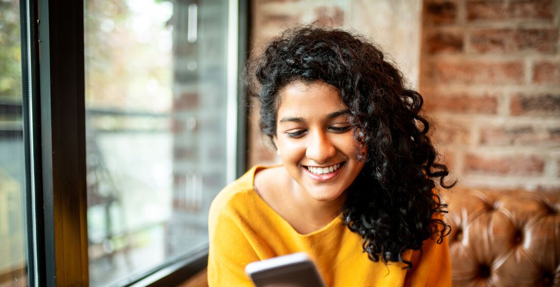 Young Indian woman using mobile phone at the bar