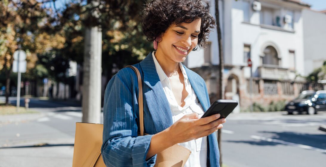 A mixed-race businesswoman reading something funny on her mobile phone on the street while going back home from work.