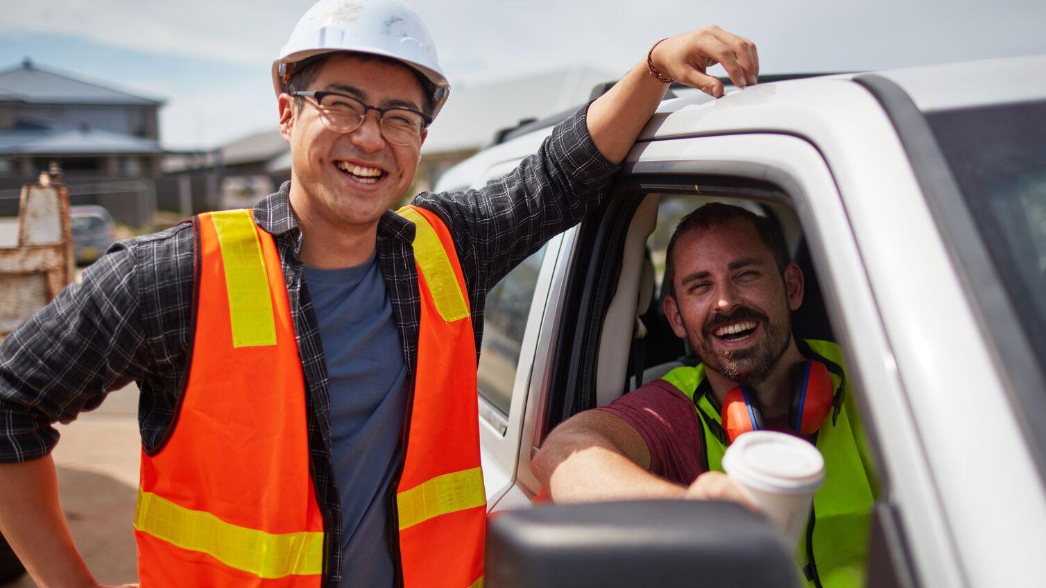 Portrait of worker smiling by colleague sitting in car. Male professionals are in reflective clothing. They are at construction site.