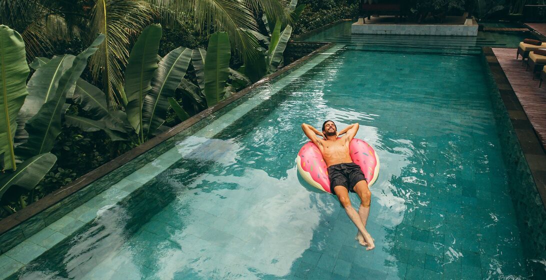 Shot of young man relaxing in resort swimming pool. Male on inflatable ring in pool.