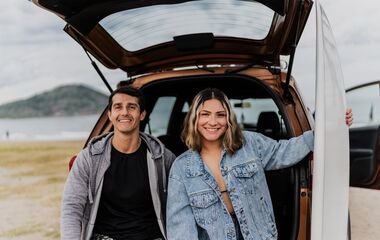 Surfer couple sitting on car trunk at the beach