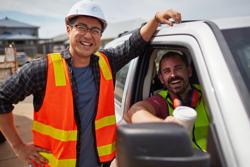 Portrait of worker smiling by colleague sitting in car. Male professionals are in reflective clothing. They are at construction site.