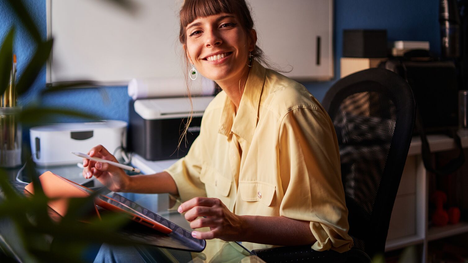 Portrait of a happy graphic designer working from home with her digital tablet looking at the camera and smiling.