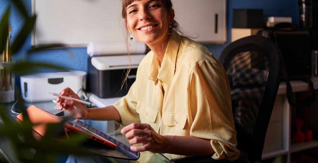 Portrait of a happy graphic designer working from home with her digital tablet looking at the camera and smiling.