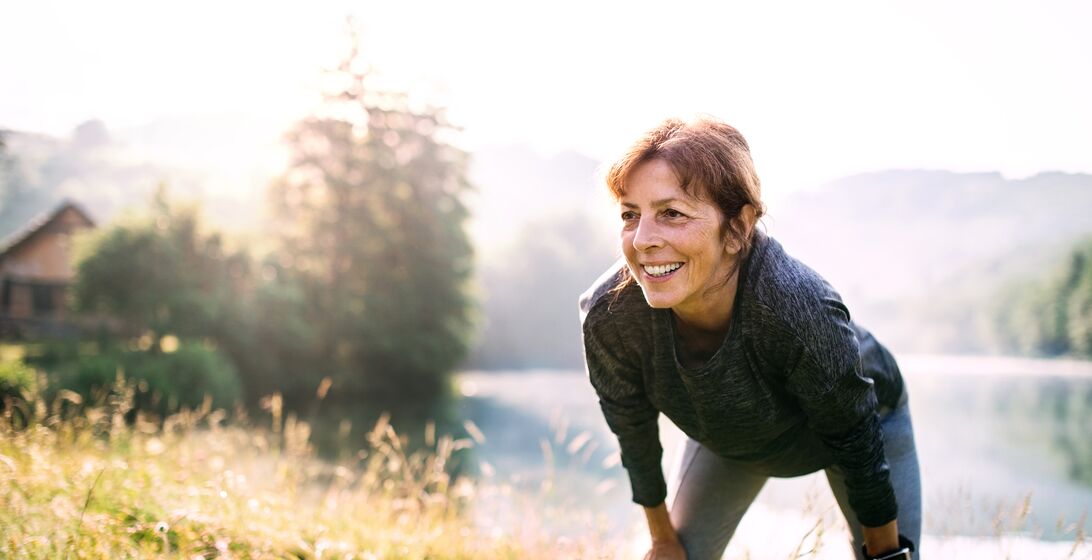 An old female sportsperson dressed in black standing by the lake outside in the countryside.