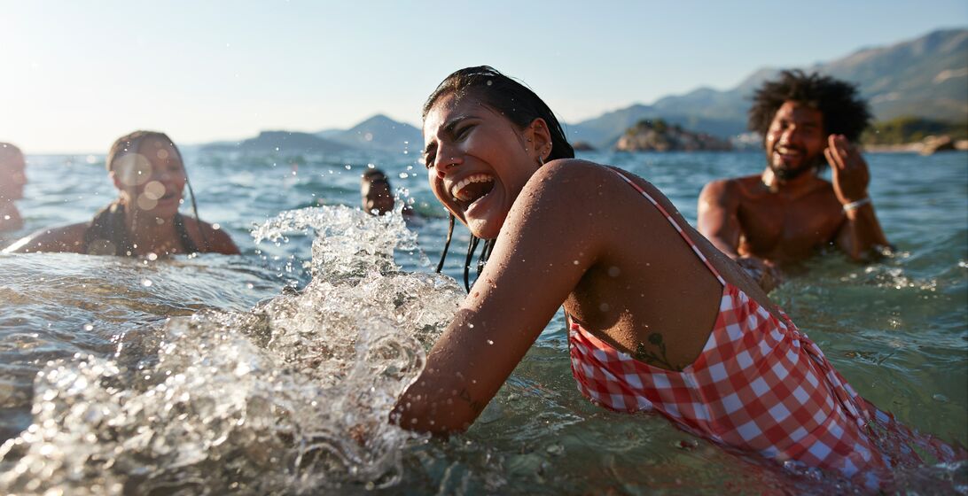Cheerful young woman splashing water while enjoying swim with friends in sea on sunny day