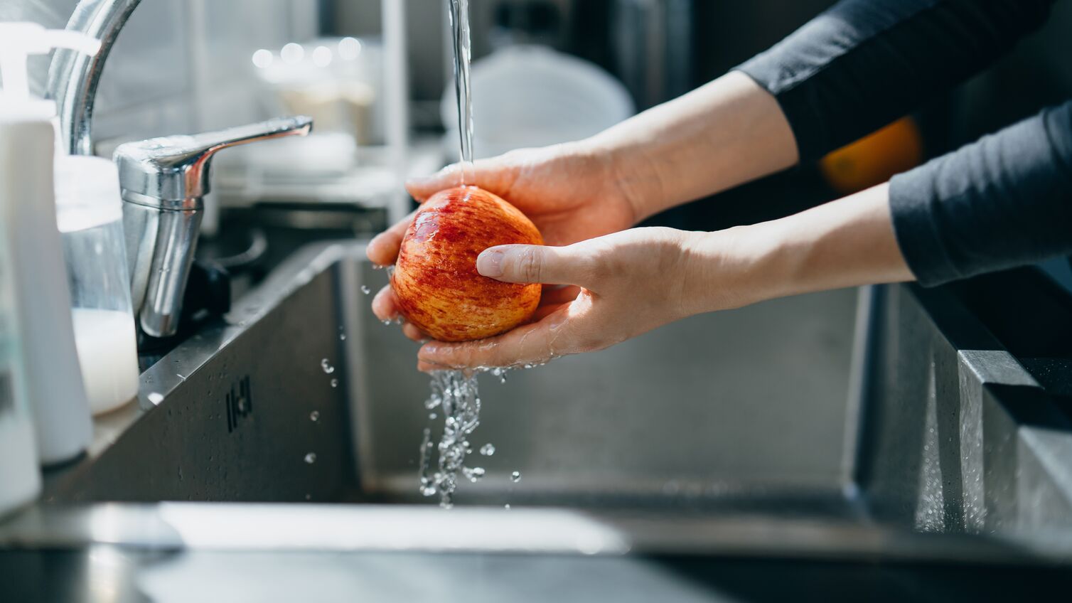 Cropped shot of woman's hand washing an red apple with running water in the kitchen sink at home