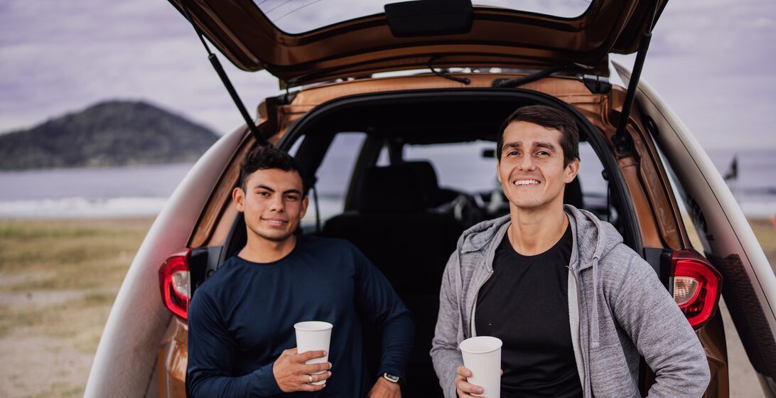 Friends sitting on car trunk at the beach