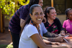 Close-up of aboriginal students and their tutor sitting outdoors in Australia. One of the female students is looking at the camera and smiling.?