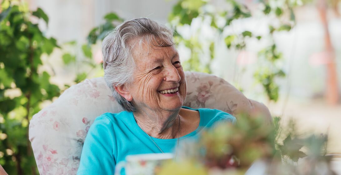A shot of a senior, Caucasian woman smiling and enjoying a cup of tea outside.