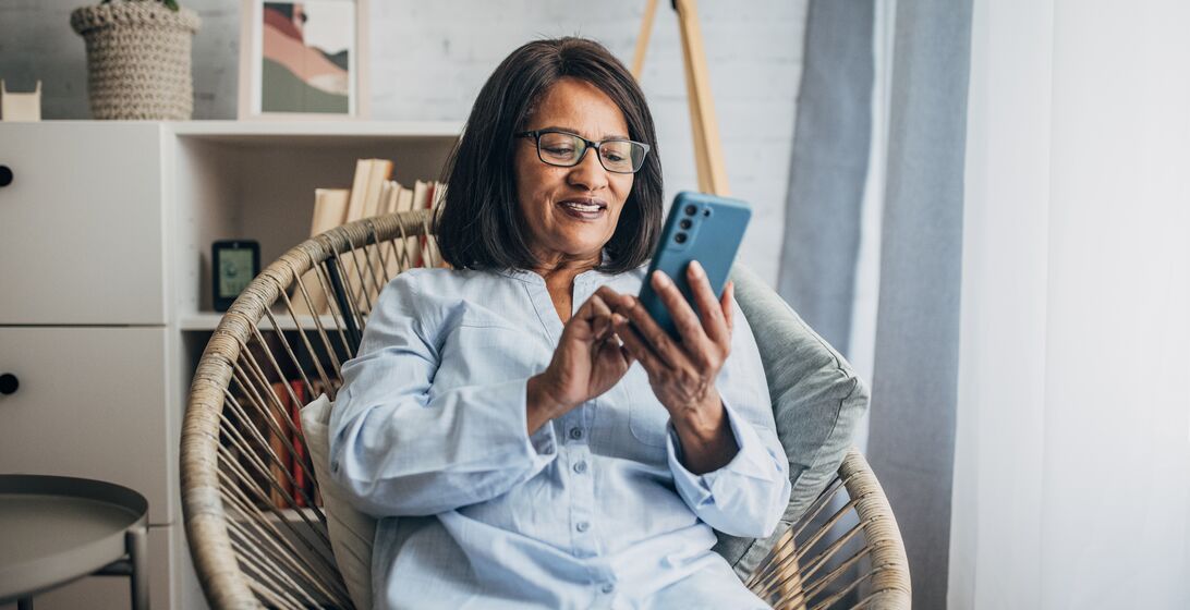 Mature black woman using smart phone while sitting in living room at home.