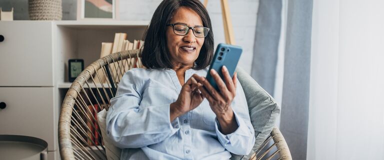 Mature black woman using smart phone while sitting in living room at home.