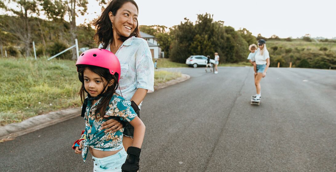 Japanese Aussie mum and daughter skateboard together in the street with other mums and kids