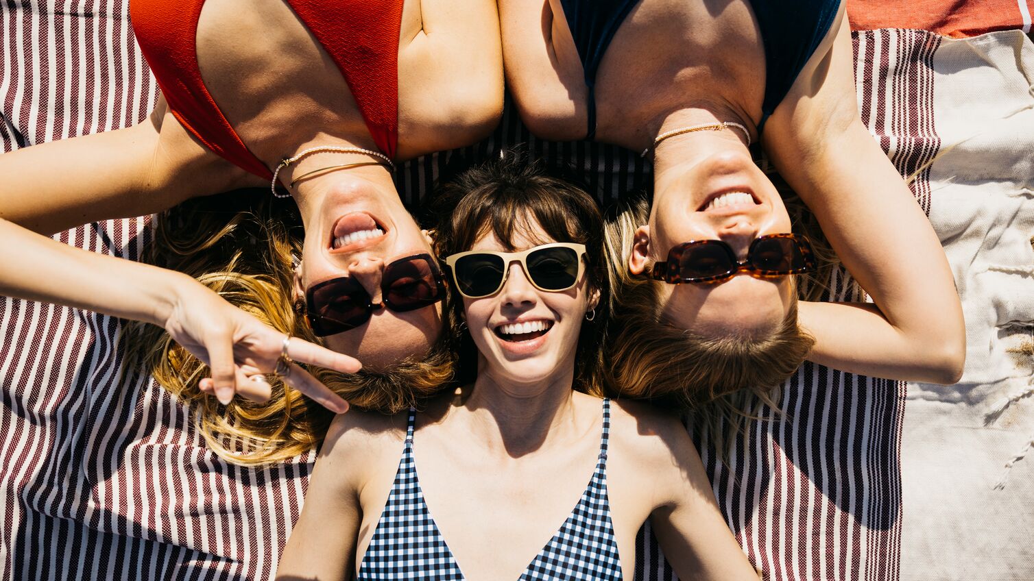 Above view of three women in swimsuits and sunglasses having a sunbath at the beach