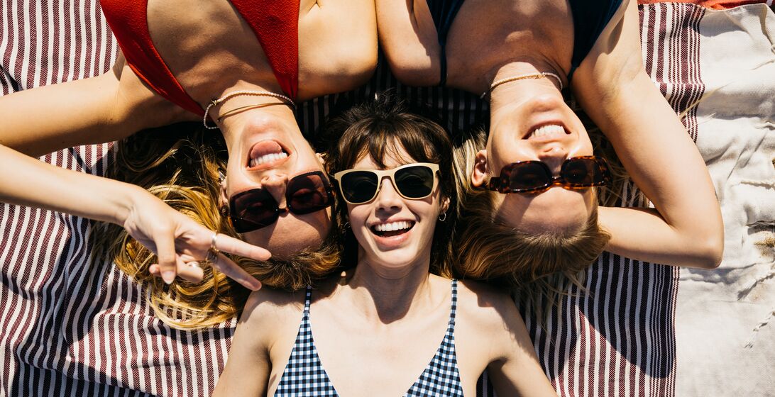 Above view of three women in swimsuits and sunglasses having a sunbath at the beach