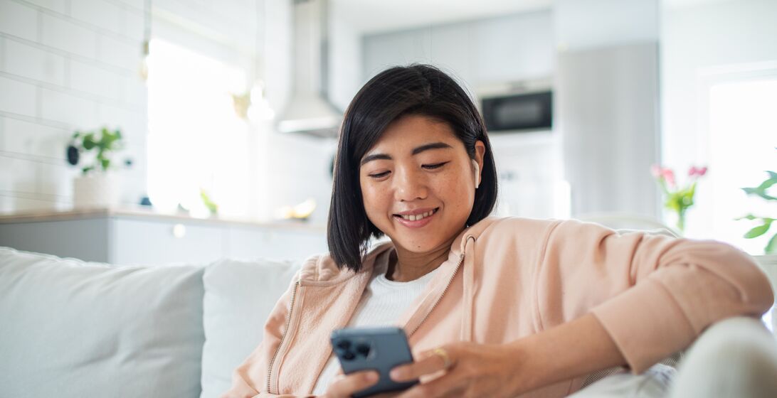 Close up of a Young woman using a smart phone while sitting on a couch in a living room