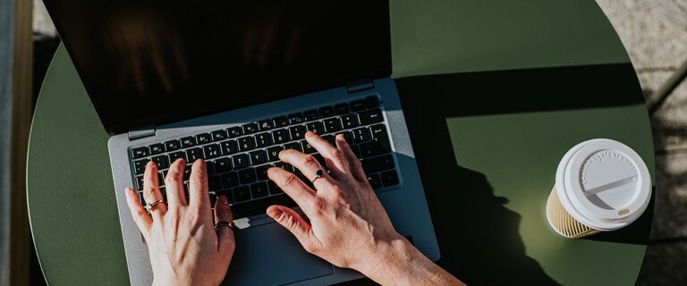 Corporate image of hands typing on a laptop keyboard in an outdoor environment, perhaps a balcony, a garden or a rooftop terrace.