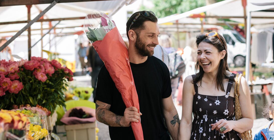 Happy couple walking through Farmer's Market. Man is carrying a bunch of Flowers.