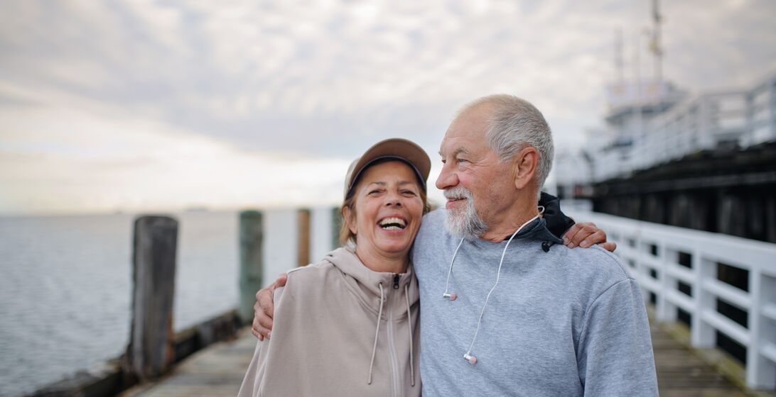 Active senior woman and man running outdoors on pier by sea.