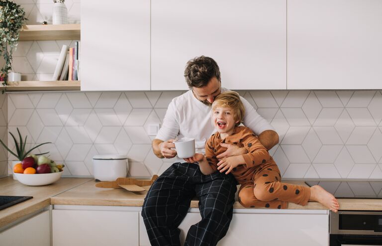 Cheerful father with his little son in kitchen in morning, bonding and looking at camera.