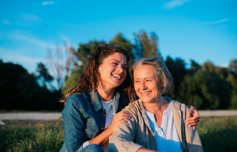 Portrait of beautiful young woman and mother sitting outside in nature. Loving mother and daughter smiling on grass lawn outdoors.