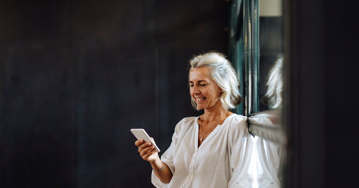 Smiling casual mature businesswoman using smartphone at the window in loft office
