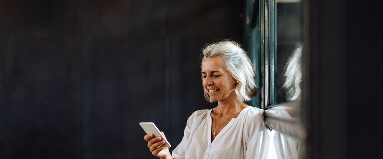 Smiling casual mature businesswoman using smartphone at the window in loft office