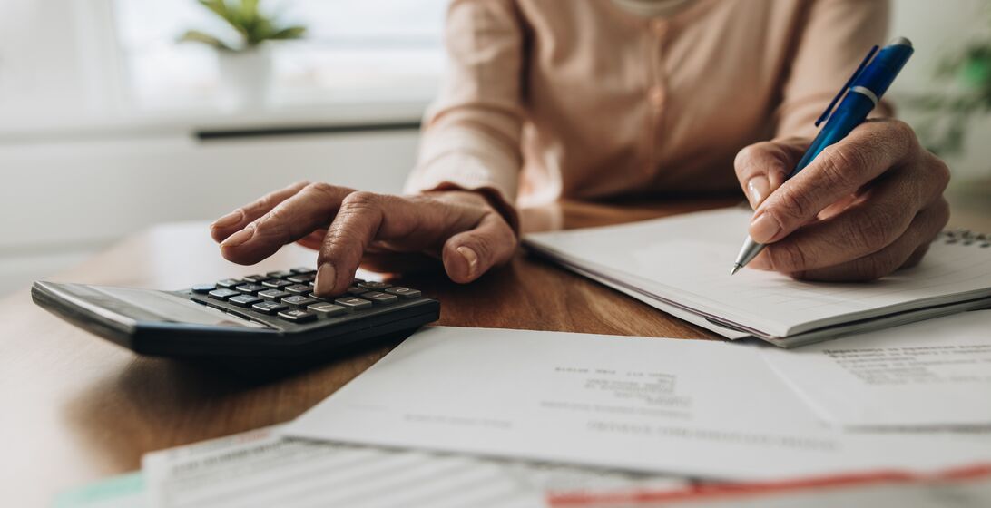 Close up of unrecognizable woman using calculator while going through bills and home finances.