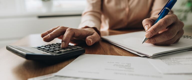 Close up of unrecognizable woman using calculator while going through bills and home finances.