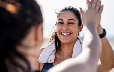 Smiling woman giving high five to her friend after exercising. Woman looking happy after a successful workout session outdoors.