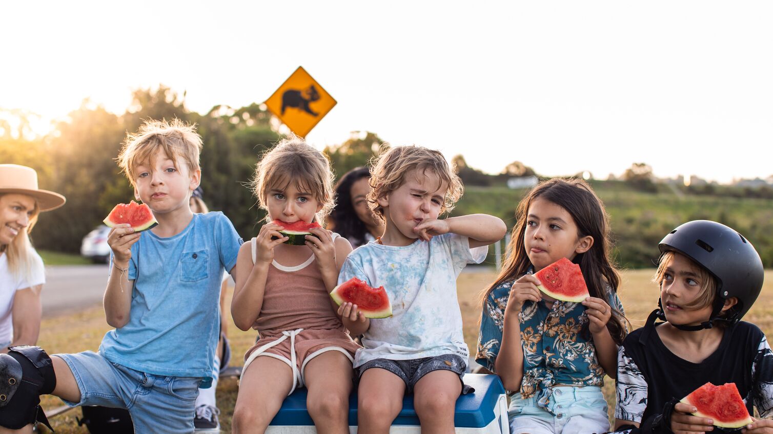 Aussie and mums and their kids eat watermelon under a koala sign
