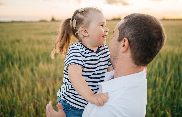 joyful child with a cochlear implant in his father's arms in a wheat field on a summer evening