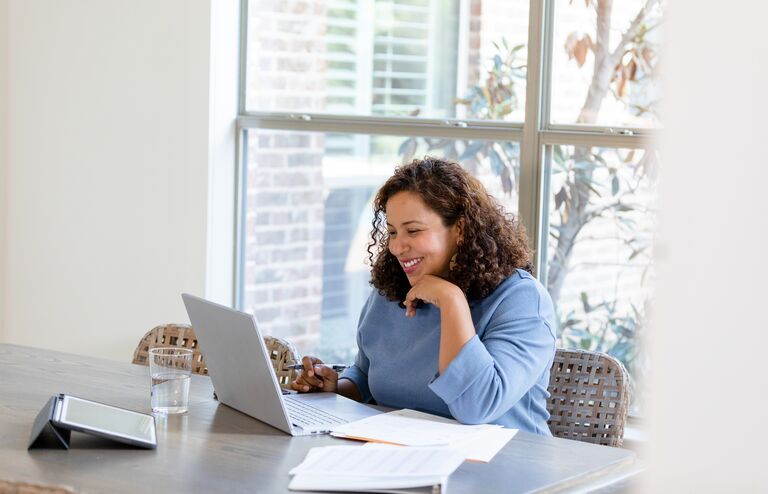 The small business owner smiles while attending a virtual meeting with her financial advisor to review upcoming changes to her taxes.