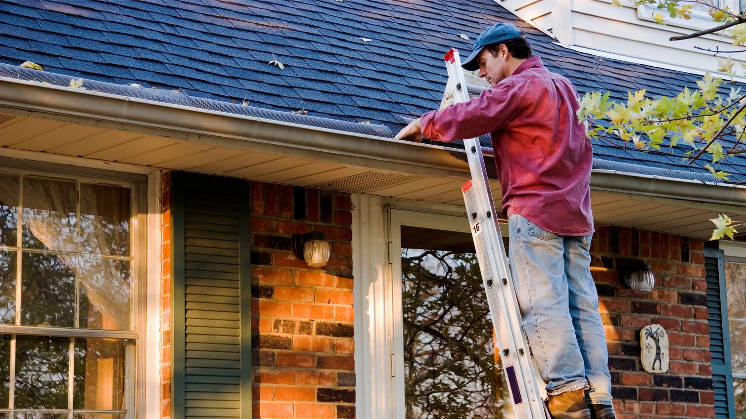 A man on a ladder cleaning his gutter